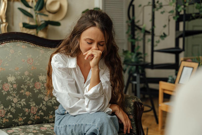Jeune femme assise sur un canapé, les yeux fermés, traversant la tristesse et le silence d’une rupture amoureuse.