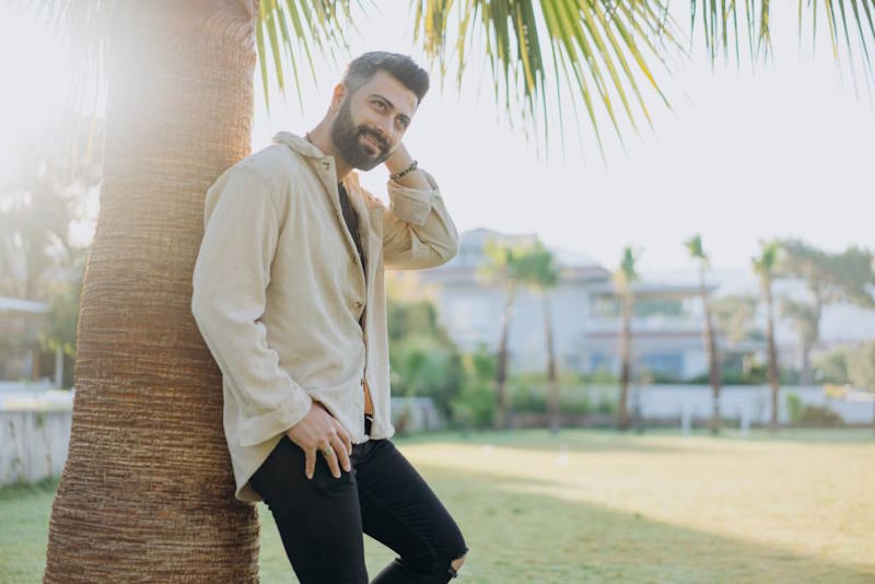 Homme pensif appuyé contre un palmier au soleil du matin, symbole d’apaisement après une rupture.