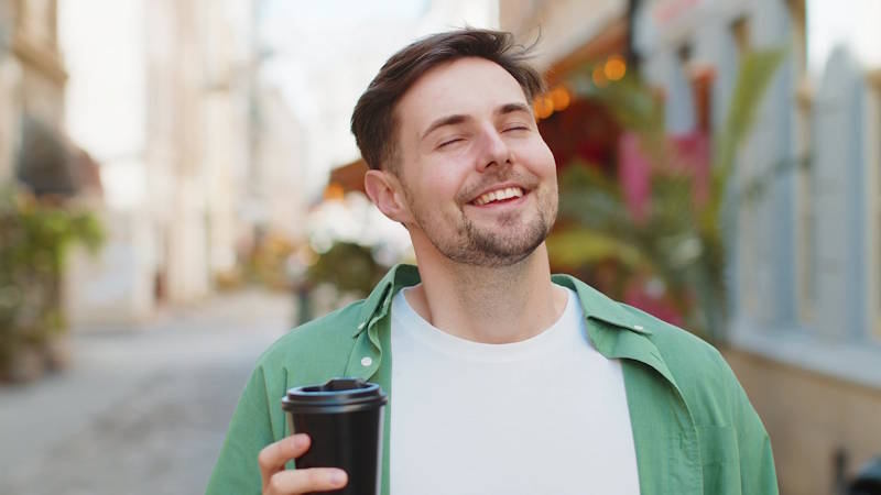 Un homme souriant marche dans la rue avec un café à la main, apaisé et confiant après avoir retrouvé son équilibre intérieur.